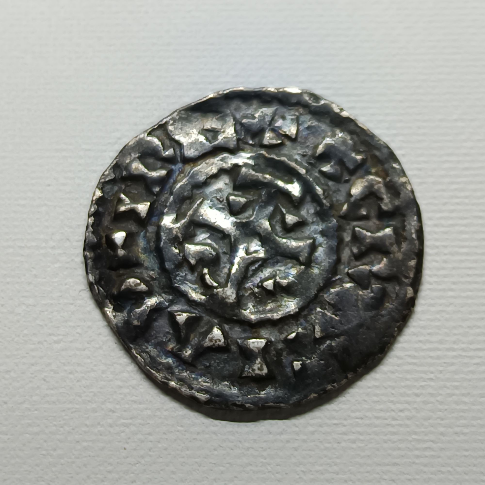 Les deniers carolingiens de Charles II le Chauve, souvent en argent, portent une croix sur une face et un monogramme royal, "KAROLVS", sur l'autre. Frappées dans de nombreux ateliers du royaume, comme Melle, Paris et Toulouse, ces monnaies témoignent du pouvoir royal et de la réforme monétaire de l'époque.