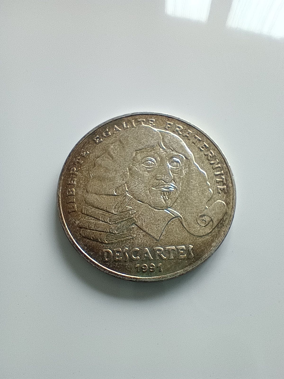 La pièce commémorative de 100 francs en argent 900‰ de 1991, émise en hommage à René Descartes, a un diamètre de 31 mm et pèse 15 g. L'avers présente le portrait de Descartes dont les cheveux se transforment en une pile de livres et un parchemin, avec la devise « LIBERTÉ ÉGALITÉ FRATERNITÉ » ; le revers montre une main pointant les douze étoiles de l'Union Européenne.