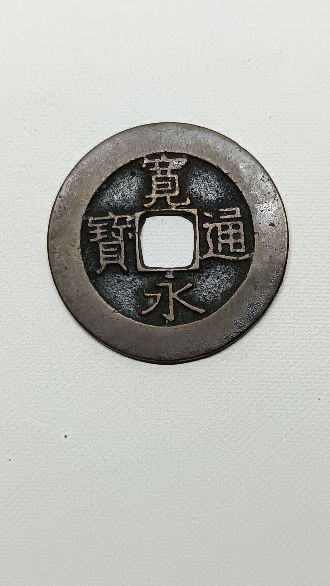 Certes. Le 4 Mon "Kan'eitsūhō" (21 vagues) est une pièce de monnaie japonaise en alliage de cuivre, frappée durant la période Edo, spécifiquement entre 1768 et 1769 (sous l'ère Meiwa). Sa valeur était de 4 Mon. Caractéristiques Numismatiques * Avers : Il porte l'inscription text{寛永通寳} (Kan'ei Tsūhō) autour d'un trou central carré. * Revers : Son trait distinctif est le motif de 21 petites vagues (ou ondulations) qui entourent le trou central. Cette caractéristique permet de la différencier de la variante ultérieure de 4 Mon qui n'a que 11 vagues. * Variétés : Il existe des variations dans la calligraphie du caractère text{寛} (Kan) au droit : * Tanbikan (text{短尾寛}) : "Kan à jambe courte," la variété la plus courante. * Chōbikan (text{長尾寛}) : "Kan à jambe longue," une variété plus rare. L'introduction de ces pièces de 4 Mon visait à compenser une pénurie de cuivre et à augmenter la valeur nominale des pièces en circulation.